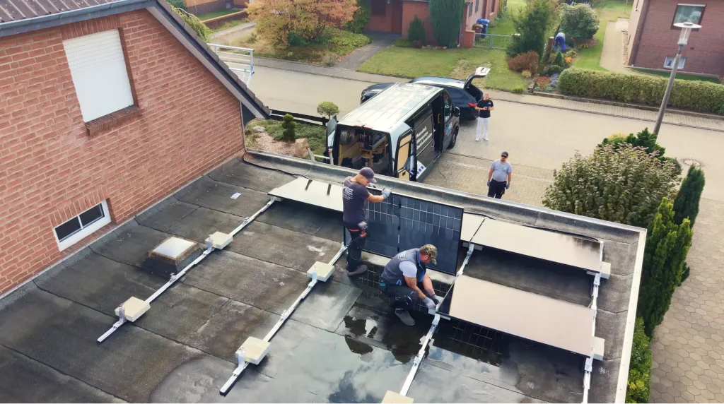 Zwei Monteure legen auf einem Flachdach PV-Module auf die Unterkonstruktion, daneben der Montagebus